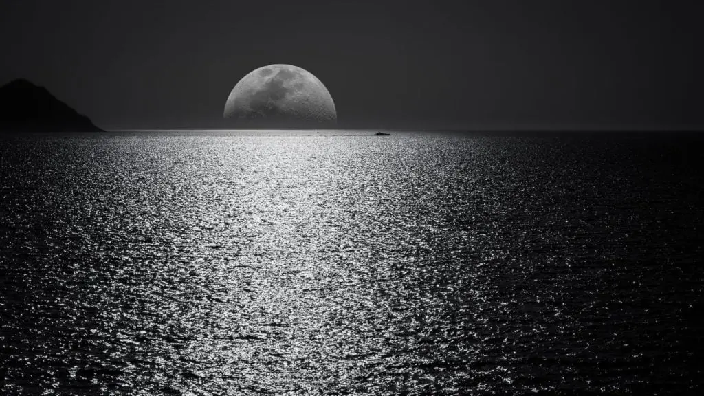 white and black moon with black skies and body of water photography during night time